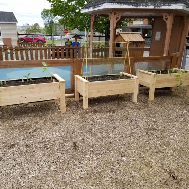 Trois bacs en bois remplis de terre sont disposés dans une cour de garderie.