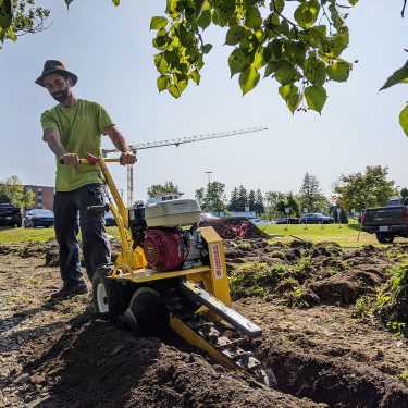 Un homme manoeuvre une machine qui creuse une tranchée dans la terre.
