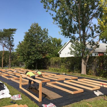 Deux hommes installent de grands cadres de bois sur une surface recouverte de géotextile.