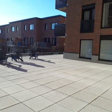 Terasse avec chaise longues d'un côté et vide de l'autre au milieu d'immeubles en briques.