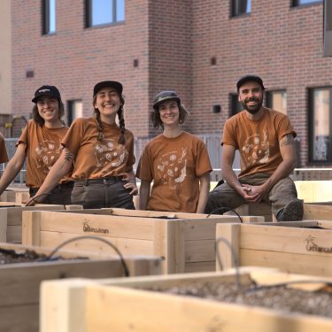 Équipe d'horticultrices et horticulteurs au milieu de bacs de jardin. Immeubles en briques en arrière plan.